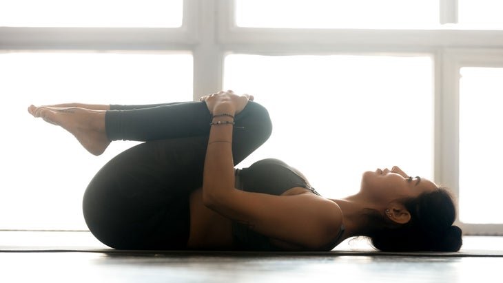 Una mujer demuestra la postura de la rodilla al pecho en yoga